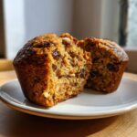 Close-up of a moist bran muffin cut in half, revealing raisins and oats inside.