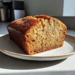 A freshly baked loaf of sugar free banana bread, sliced to show the moist crumb, sitting on a light-colored plate.
