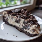A generous slice of creamy Oreo cheesecake with a dark chocolate crust and topped with crushed cookies.