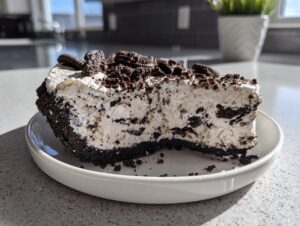 A thick slice of creamy Oreo pie with a dark chocolate crust, topped with crushed Oreos.