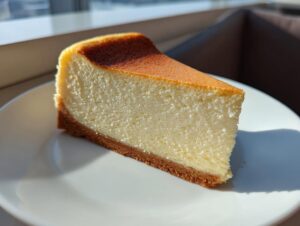 A perfect, crack-free slice of creamy new york cheesecake with a graham cracker crust on a white plate.