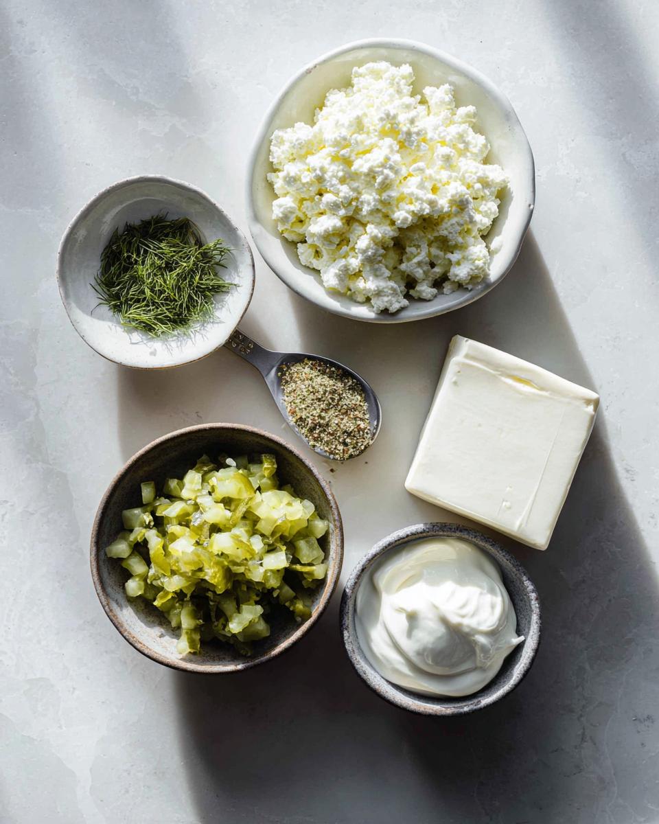 Overhead shot of ingredients for pickle dip, including cottage cheese, chopped pickles, cream cheese, and dill.