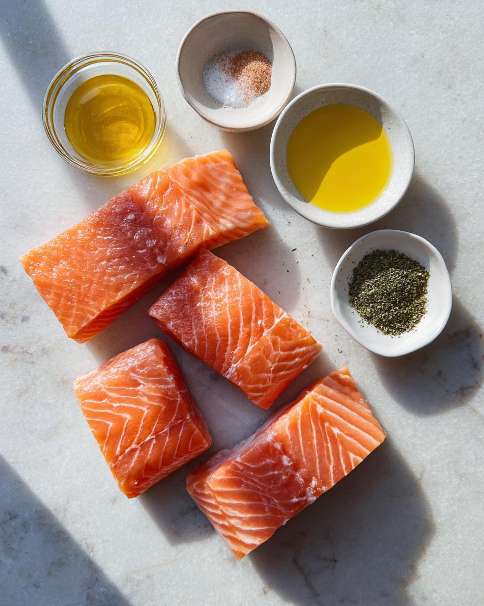 Four raw salmon fillets displayed with olive oil, salt, and dried herbs for seasoning.