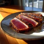 Four slices of perfectly cooked Seared Ahi Tuna with a dark sesame seed crust on a light plate.