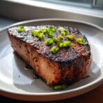 A perfectly seared tuna steak, glistening with glaze and topped with fresh green onion slices, ready to eat.
