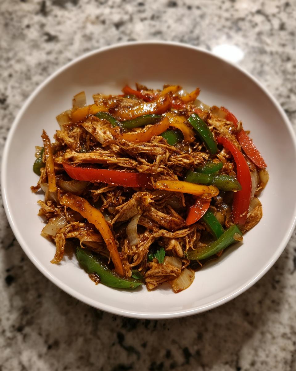 Shredded chicken mixed with colorful bell peppers and onions, the filling for crockpot chicken fajitas, served in a white bowl.