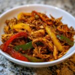 Close-up of shredded, seasoned chicken mixed with sliced red, yellow, and green peppers, ready for crockpot chicken fajitas.