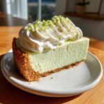 A perfect slice of creamy, light green key lime cheesecake topped with whipped cream and lime zest.