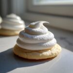 Close-up of a soft sugar cookie topped with a tall swirl of bright white, fluffy sugar cookie icing.