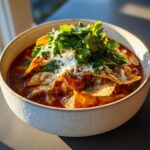 Close-up of a rich, red broth tortilla soup recipe garnished generously with shredded white cheese, crispy tortilla strips, and fresh cilantro.