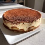 A whole, round tiramisu recipe dessert with creamy layers and a heavy dusting of cocoa powder on top.