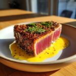 A thick slice of perfectly seared air fryer tuna steak, crusted with spices and served over a bright yellow sauce.