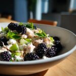 A close-up of blackberry cottage cheese chicken salad featuring shredded chicken, cottage cheese, celery, and fresh blackberries, garnished with mint.