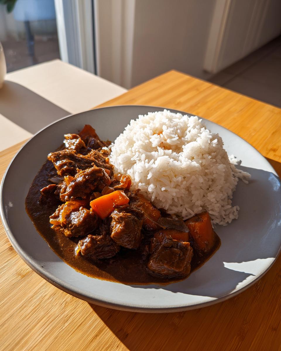 A plate featuring rich brown stew chicken and white rice, served on a wooden table in bright sunlight.