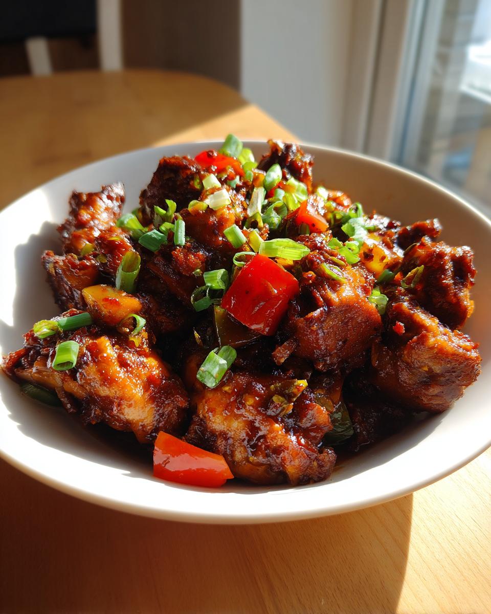 Close-up of rich, dark brown stew chicken pieces garnished with chopped green onions and red bell peppers.