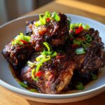 Close-up of glossy brown stew chicken jamaican crock pot pieces garnished with scallions and red pepper.