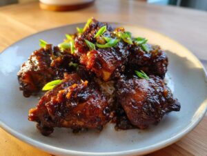 Close-up of rich, dark brown stew chicken jamaican recipe pieces served over white rice and garnished with green onions.