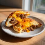 Two halves of a baked cheeseburger pockets biscuits showing the ground beef and melted cheese filling.