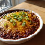 Close-up of a hot chili cream cheese dip topped with melted cheddar and sliced green onions.