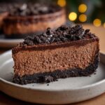 Close-up of a rich slice of chocolate cheesecake with a dark cookie crust and crumbled topping.