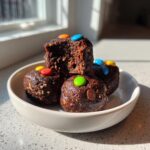 A stack of four rich, dark chocolate cosmic brownie protein bites topped with colorful candy-coated chocolates.