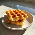 A stack of two golden brown cottage cheese waffles healthy served on a speckled white plate in bright sunlight.