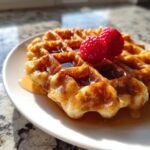 Close-up of a golden brown cottage cheese waffles low carb drizzled with syrup and topped with fresh raspberries.