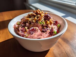 A close-up of pink cranberry jalapeno cream cheese dip topped with pecans and cranberries in a white bowl.