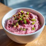 Close-up of vibrant pink cranberry jalapeno cream cheese dip topped with pecans, cranberries, and green onions.