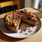 A slice removed from a rich dubai chocolate cheesecake topped with whole and crushed hazelnuts.