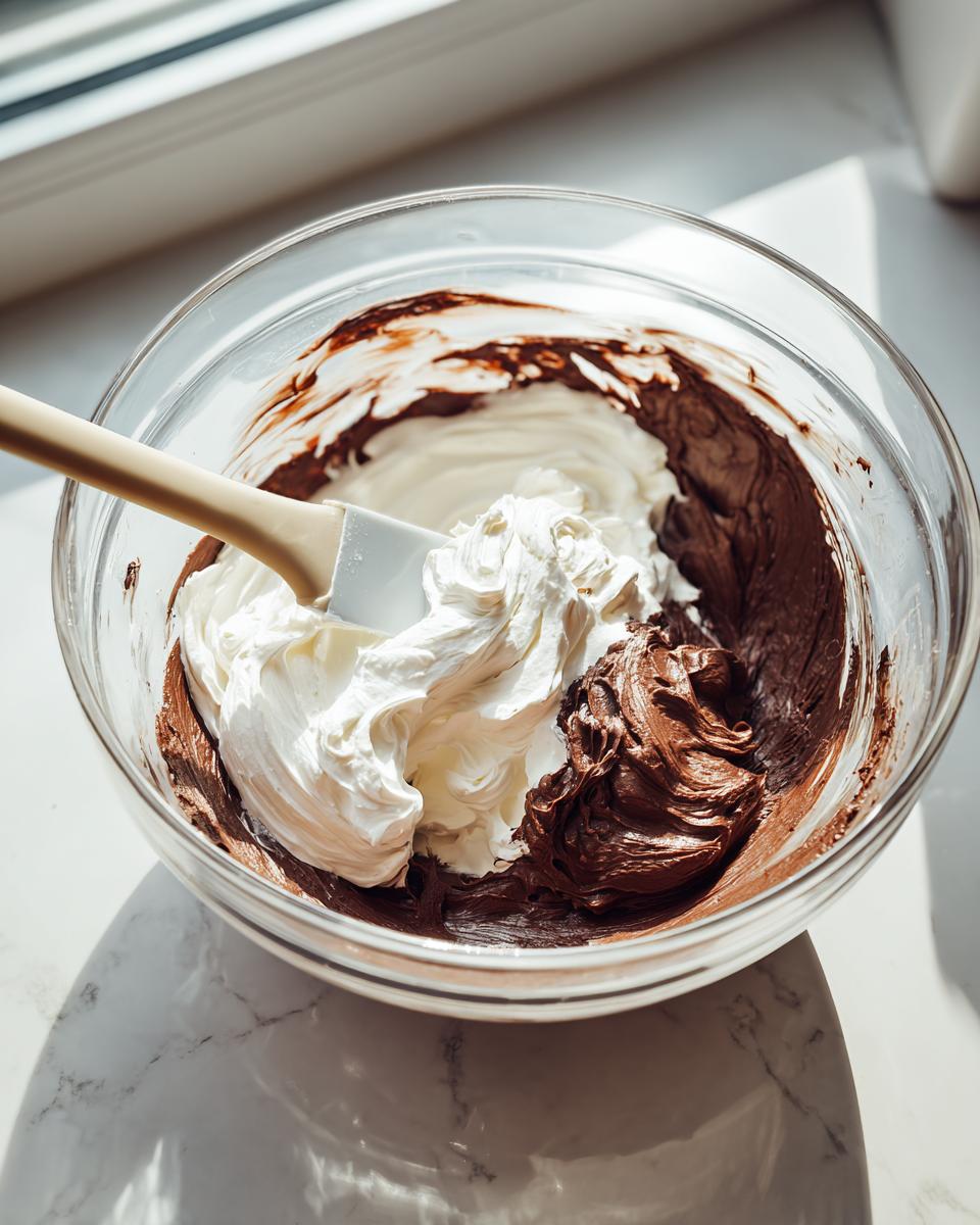 Mixing rich chocolate base with whipped cream using a spatula for no bake chocolate cheesecake filling.