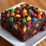 A close-up of a fudgy cosmic brownies square topped with melted chocolate frosting and colorful candy coated chocolates.