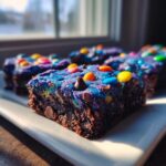 A close-up of a rich, dark square of healthy cosmic brownies topped with vibrant blue frosting and colorful candies.