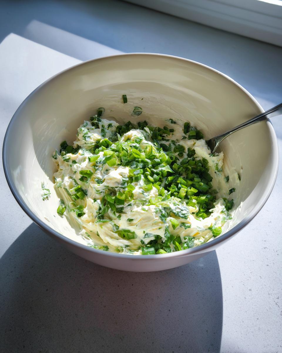Cream cheese mixture being combined with chopped green onions for jalapeno cream cheese dip in a white bowl.