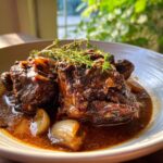 Close-up of rich, dark brown stewed meat, possibly authentic Jamaican brown stew chicken, served in a bowl with onions and thyme garnish.
