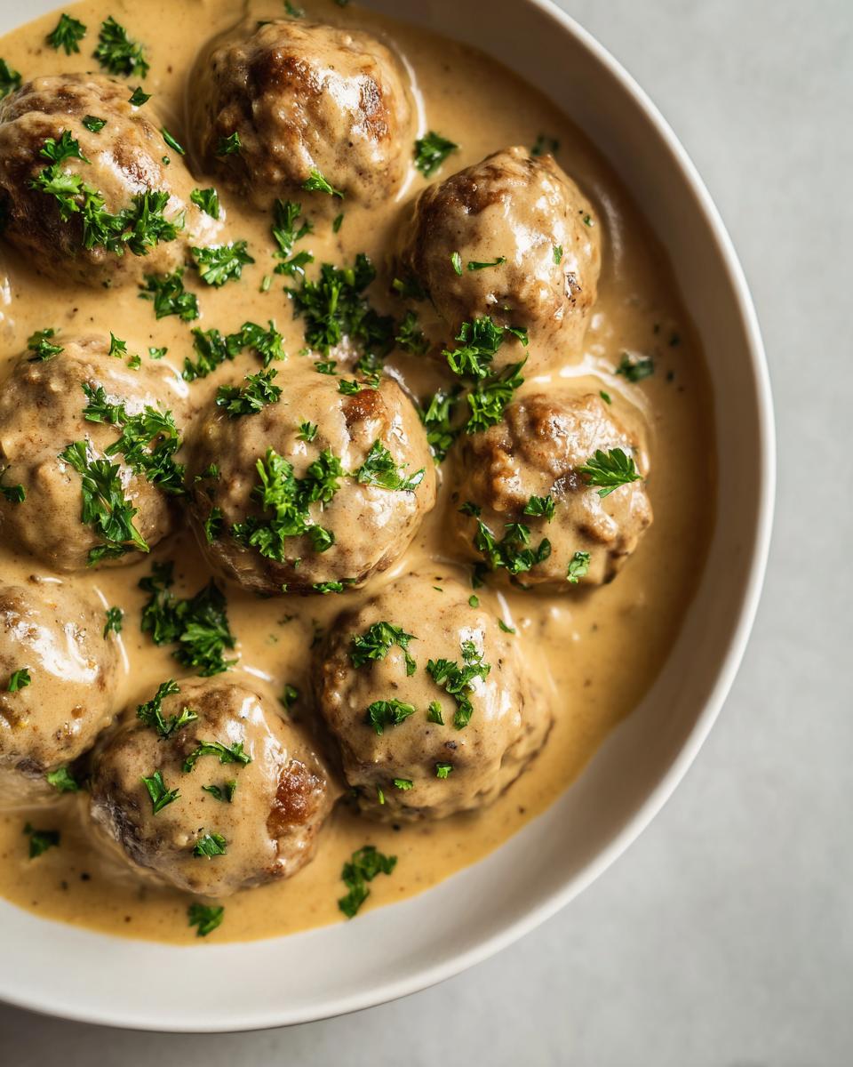 Close-up of juicy Swedish meatball recipe crockpot meatballs covered in creamy brown gravy and topped with fresh parsley.