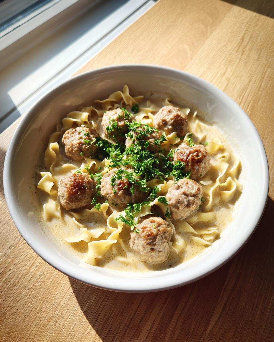 A bowl of creamy swedish meatball soup featuring meatballs, egg noodles, and fresh parsley garnish.