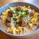 Close-up of a bowl of swedish meatball soup featuring browned meatballs, egg noodles, and creamy sauce, topped with parsley.
