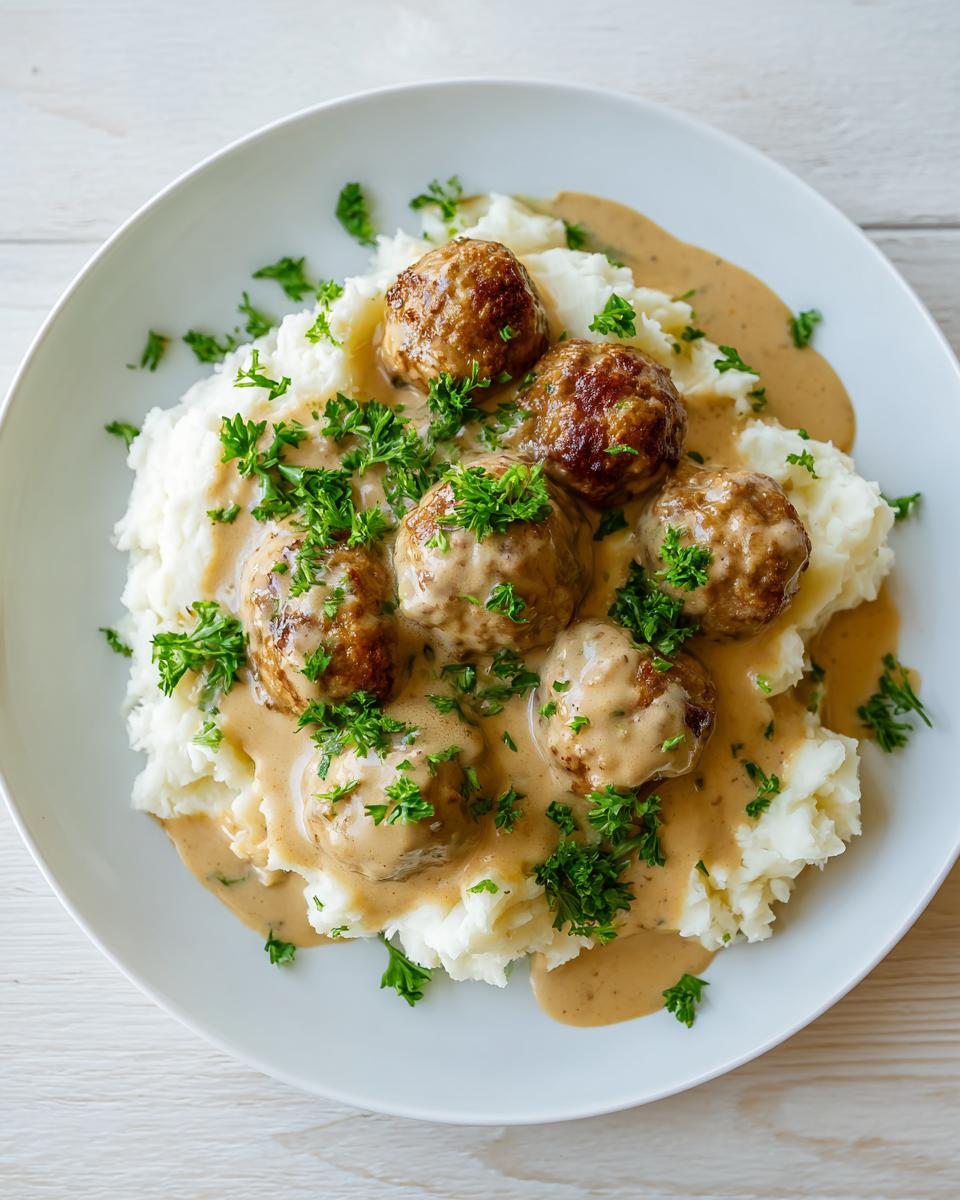 Five browned Swedish meatballs served over creamy mashed potatoes and smothered in brown gravy, garnished with fresh parsley.