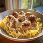 A bowl of savory swedish meatballs over egg noodles covered in creamy gravy, lit by natural light.