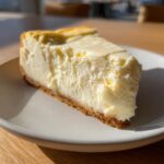 A thick slice of creamy white chocolate cheesecake with a graham cracker crust, sitting on a light plate.
