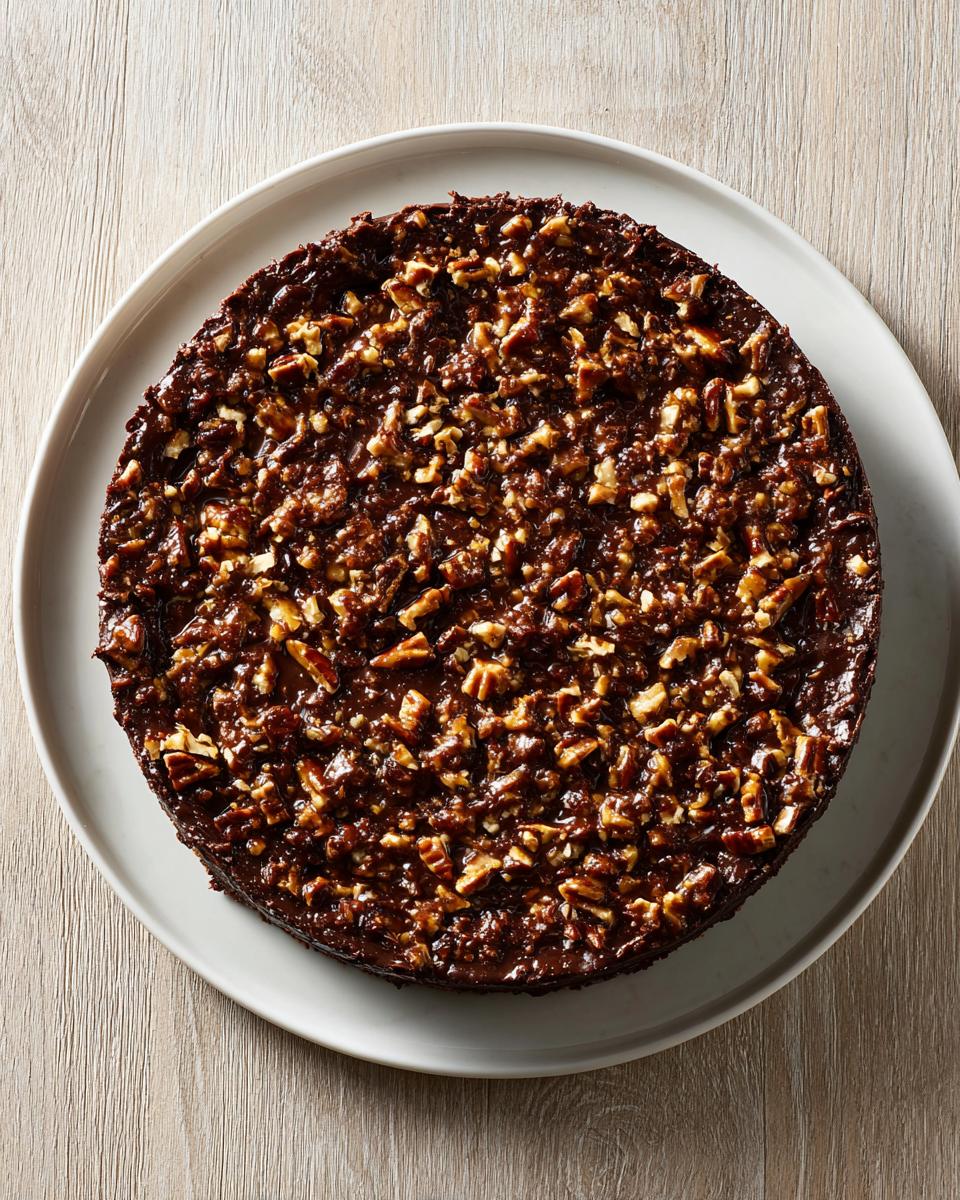 Overhead view of a whole german chocolate cheesecake covered in rich chocolate frosting and chopped pecans.